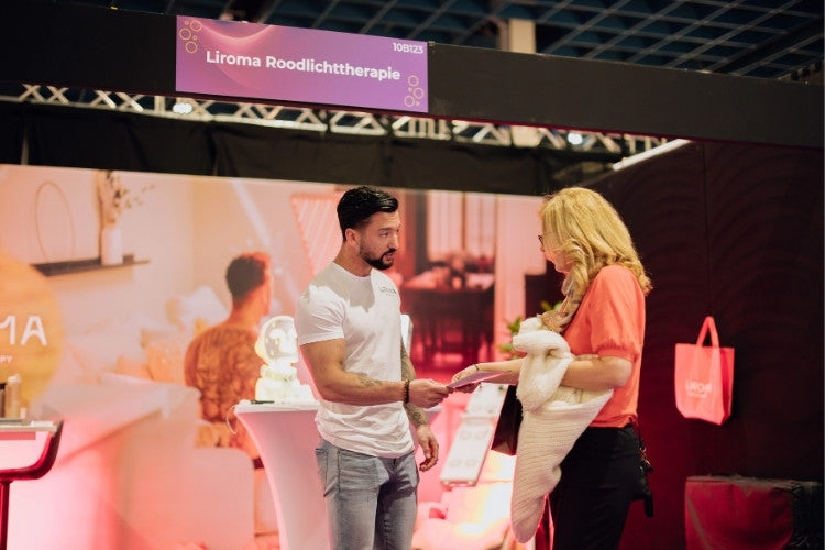 Bezoeker ontvangt uitleg bij de Liroma roodlichttherapie stand tijdens een beauty beurs