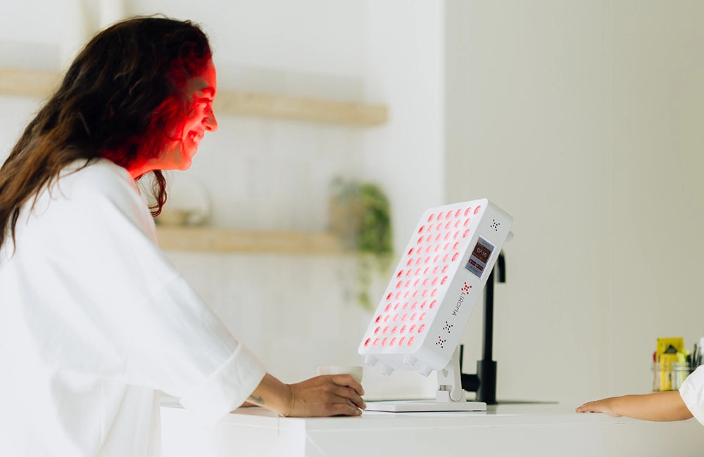 Frau behandelt ihr Gesicht mit der Liroma Compact Rotlichtlampe am Tisch