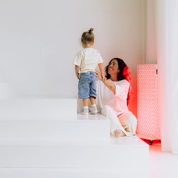 Vrouw met kind naast de Liroma Elite rood licht therapie lamp in de woonkamer